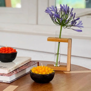 Decorative candles in black bowls with a purple flower in a glass vase on a wooden surface.