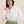 Woman wearing a white button-up shirt and green pants with a beige belt against a beige background