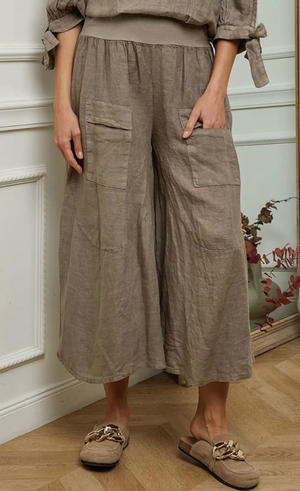 Person wearing beige linen pants standing in a room with a decorative wall and plant.