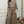 Woman wearing a brown top and wide leg linen pants standing in a room with a mirror and decorative items.