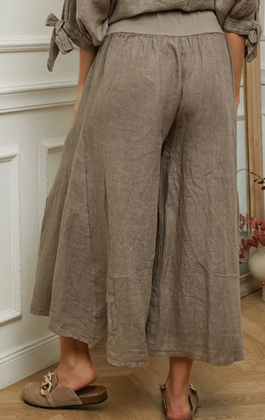 Person wearing brown linen pants standing in a room with a mirror and decorative items.