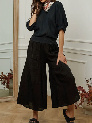 Woman wearing a black outfit with wide-leg pants in a room with decorative elements.