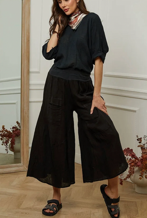 Woman wearing a black outfit with wide-leg pants in a room with decorative elements.