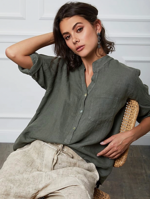 Woman wearing a green henley shirt and beige pants sitting on a wicker chair.