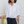 Woman wearing a white henley shirt and navy pants holding a straw bag against a white background