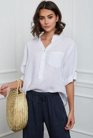 Woman wearing a white henley shirt and navy pants holding a straw bag against a white background