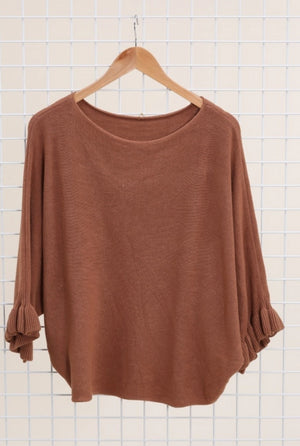 Light brown dolman sweater on a hanger against a tiled wall background