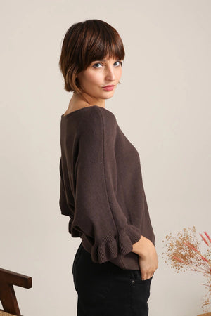 Woman wearing a brown dolman sweater against a plain background