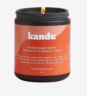 Kandu candle with a lit wick and orange label