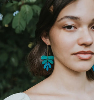 Woman wearing teal leaf-shaped earrings with a blurred green background