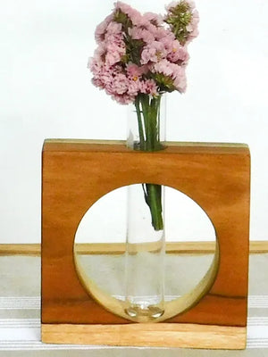 Wooden vase with circular cutout holding pink flowers on a white background