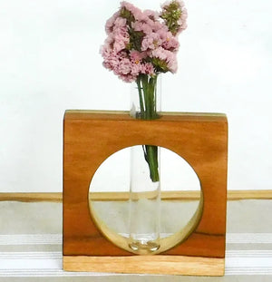 Wooden vase with circular cutout holding pink flowers on a white background