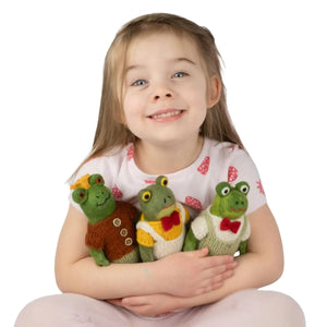 Young girl holding three knitted frog toys against a white background