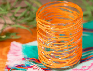 Orange glass with decorative pattern on a colorful fabric background