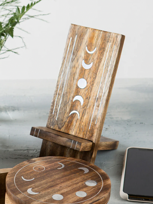 Wooden phone stand with moon phase design on a light surface.