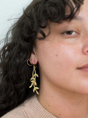 Close-up of a person wearing gold leaf earrings with a neutral background