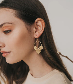 Close-up of a woman wearing gold hoop earrings with heart-shaped pendants.
