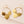 Gold hoop earrings with leaf-shaped pendants on a light pink background