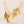 Gold leaf-shaped earrings on a light pink background
