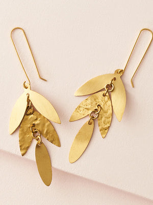 Gold leaf-shaped earrings on a light pink background