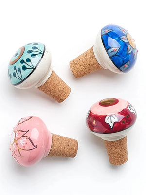 Four painted decorative mushroom-shaped bottle stoppers with cork bases on a white background