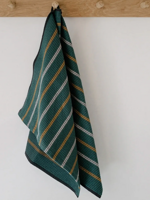 Striped green towel hanging on a wooden hook against a white wall