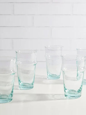 Set of six clear glasses on a white surface with a white tiled wall background