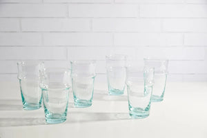 Set of six clear glasses on a white surface with a white tiled wall background