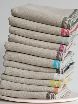 Stack of folded napkins with colorful stripes on a white plate against a light gray background