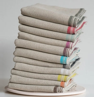 Stack of folded napkins with colorful stripes on a white plate against a light gray background