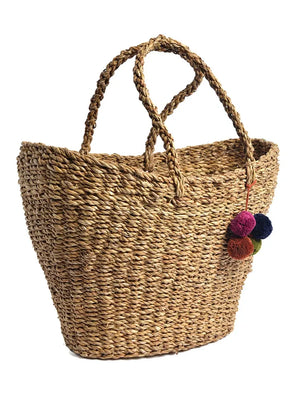 Woven straw tote bag with colorful pom-poms on a white background