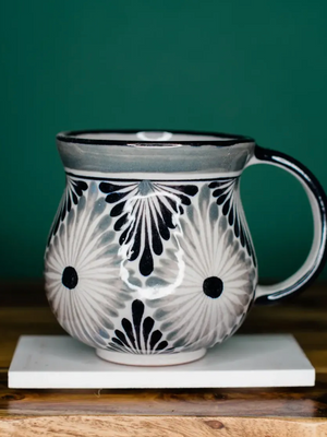 Ceramic mug with black and white pattern on a wooden surface and green background