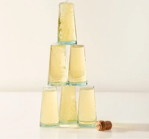 Clear glass tumblers stacked in a pyramid with a cork on a light background