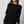 Woman wearing a black sweater and blue jeans against a white paneled wall.