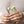 Close-up of hands holding a small plant with white flowers, wearing gold stacking rings.
