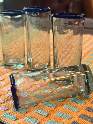 Four shot glasses with blue rims on an orange and green patterned tablecloth.