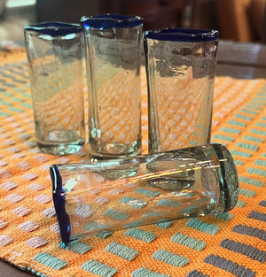 Four shot glasses with blue rims on an orange and green patterned tablecloth.