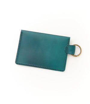 Teal leather cardholder with a gold ring on a white background