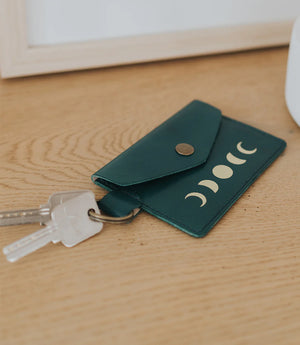 Green leather keychain with moon phase design on a wooden surface