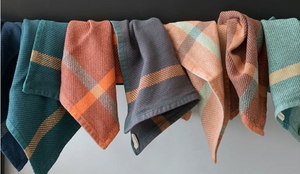 Set of folded plaid washcloths in various colors on a white surface.