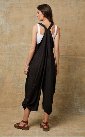 Woman wearing a black overalls and white top against a beige wall