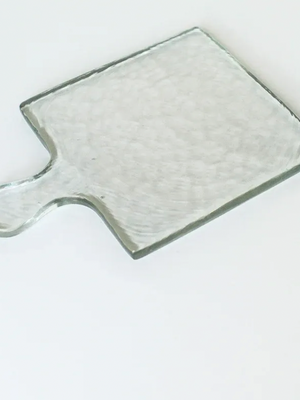 Clear glass cutting board with handle on a white background