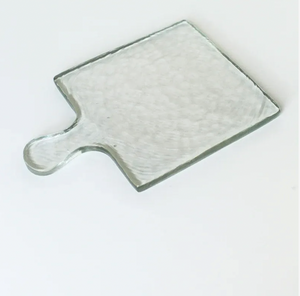 Clear glass cutting board with handle on a white background