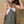 Woman wearing a green overalls with a white top against a beige background