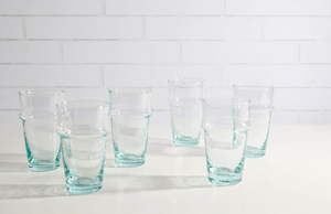 Set of six clear glass tumblers on a white surface with a white tiled wall background