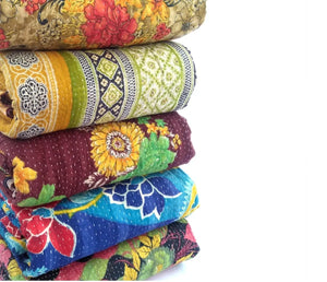 Stack of colorful kantha quilts with various patterns on a white background