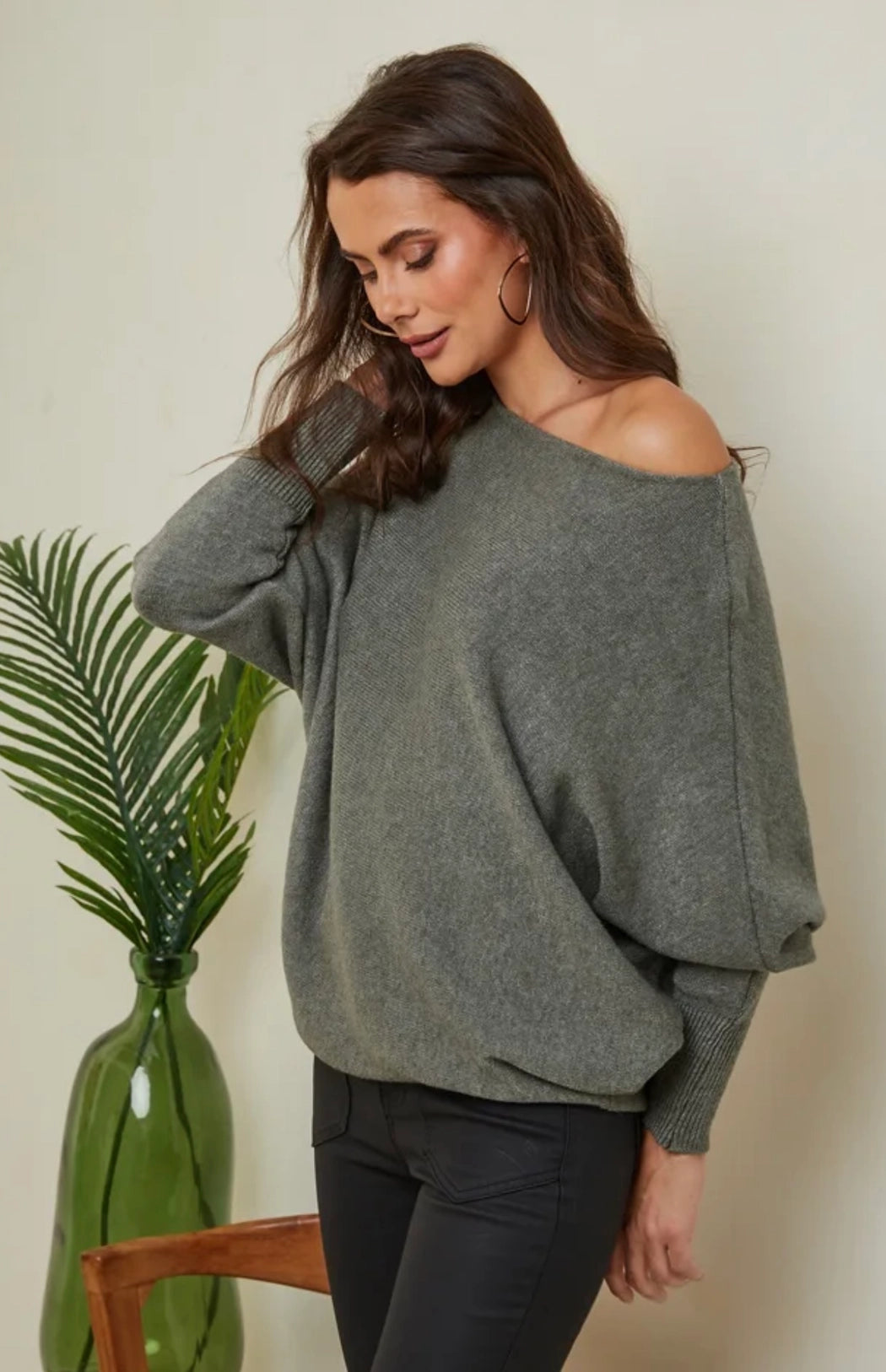 Woman wearing a gray off-shoulder sweater with a plant in the background