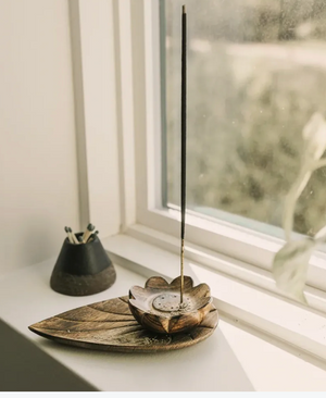 Handcarved wooden incense holder with a single incense stick on a windowsill.