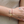 Close-up of a wrist wearing a gold bracelet with a small charm, against a neutral background.
