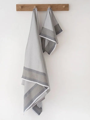Two gray towels with decorative patterns hanging on a wooden rack against a white wall.